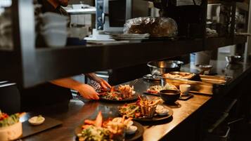 A kitchen area with a chef preparing food, various dishes on the counter, and kitchen appliances.