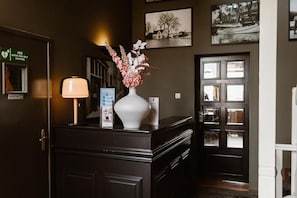Balcão de recepção com um vaso de flores, uma luminária e folhetos informativos.