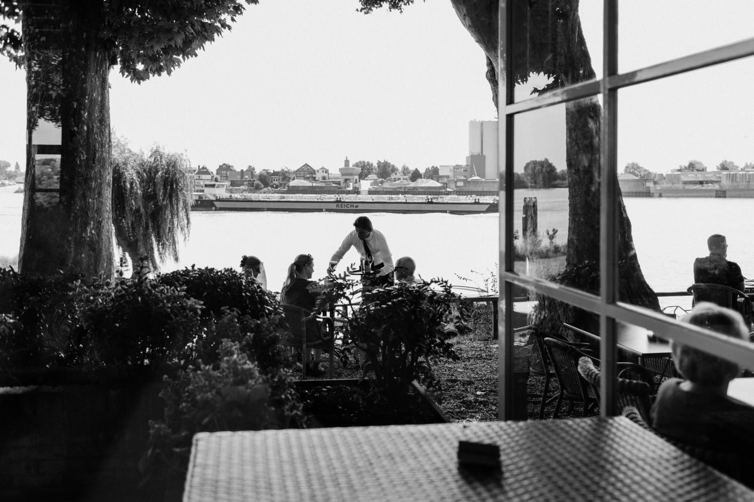 A room with a large window overlooking a body of water, a table with a chair, and a view of a cityscape in the distance.