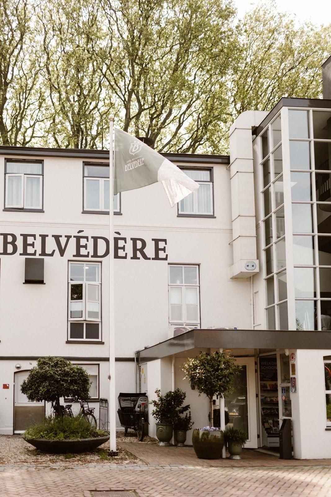 A building with the sign 'BELVEDERE' and a flagpole with a flag. There are potted plants and a bicycle outside.