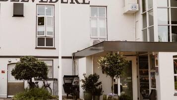 A building with the sign 'BELVEDERE' and a flagpole with a flag. There are potted plants and a bicycle outside.