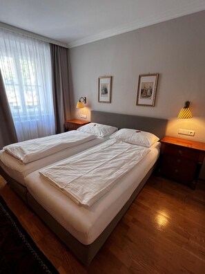 A hotel room with two beds, a wooden floor, and two bedside lamps. - Hotel Gv Sser Brv U (Wels)