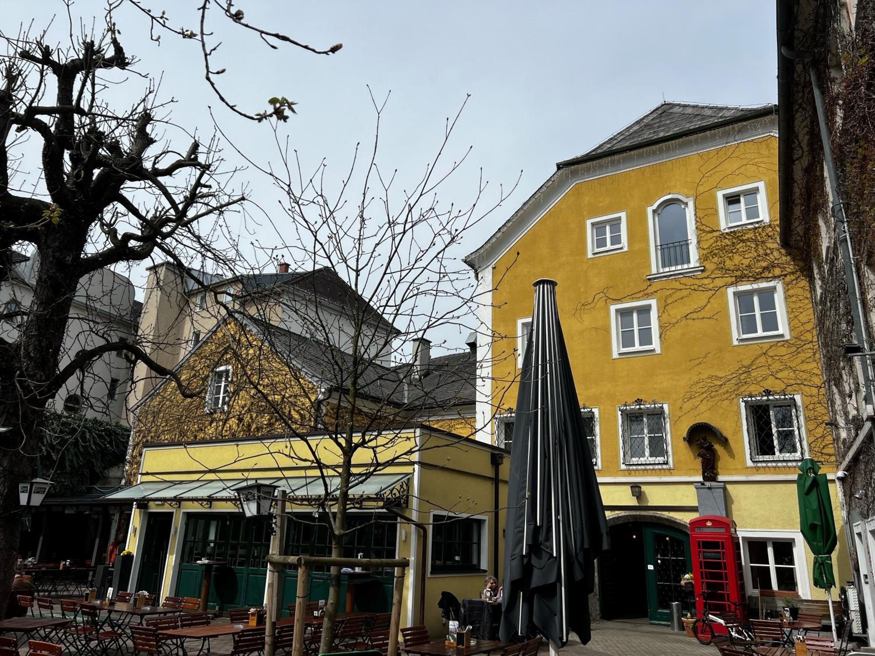 A yellow building with a green door, outdoor seating, and a red telephone booth.