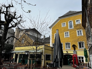 Ein gelbes Gebäude mit grüner Tür, Außenbestuhlung und einer roten Telefonzelle.
