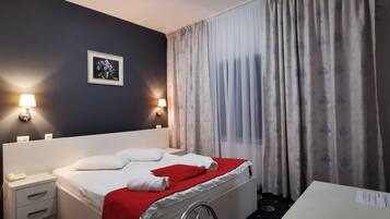 A hotel room with a bed, bedside tables, a lamp, a painting, and a window with curtains.