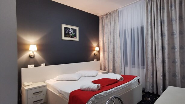 Habitació d'hotel amb un llit, taules de nit, una làmpada, un quadre i una finestra amb cortines.