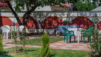 An outdoor seating area with tables and chairs, surrounded by a garden with a brick pathway.