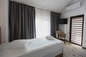 A hotel room with a bed, a chair, a TV, and a window with curtains.