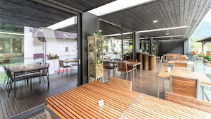 Un restaurant moderne avec des tables et des chaises en bois, des murs en verre et une vue sur l’extérieur.