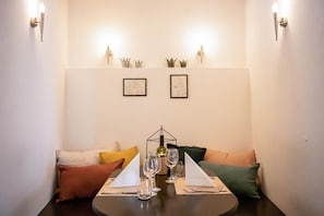 Un coin repas avec une table ronde dressée pour deux personnes, deux œuvres d’art encadrées accrochées au mur et une couronne décorative au-dessus des œuvres d’art.