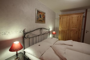Une chambre à coucher avec un lit, une table de chevet avec une lampe, une porte en bois et un mur orné d’un tableau.