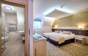 Un dormitorio moderno con una cama grande, mesitas de noche, un escritorio con silla, y un baño con ducha, inodoro y lavabo.