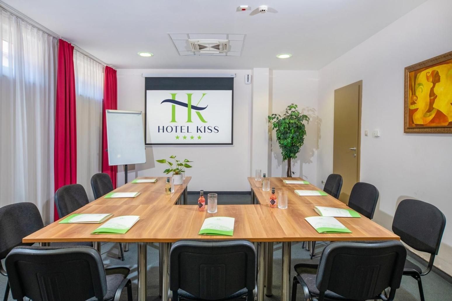 A conference room with a long table, chairs, a projector screen, and a plant.