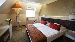 Habitación de hotel con una cama, una mesita de noche, una lámpara, un ventanal y un detalle decorativo en la pared.