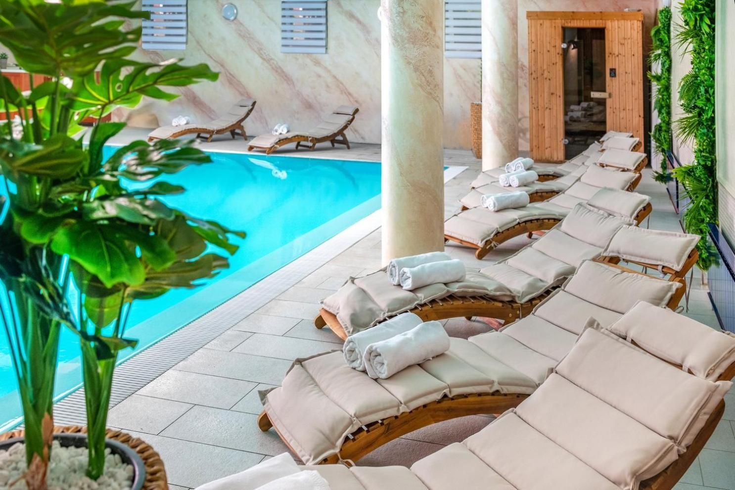 A poolside area with lounge chairs and towels, a wooden sauna door, and a plant.