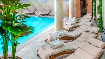 A poolside area with lounge chairs and towels, a wooden sauna door, and a plant.
