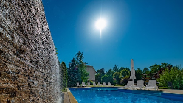 Una piscina con una fuente en un lateral, rodeada de sillones de descanso y un cielo despejado.