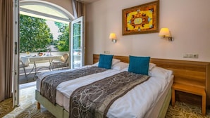 Habitación de hotel con una cama grande, dos lámparas de noche, un cuadro en la pared y un balcón con mesa y sillas.