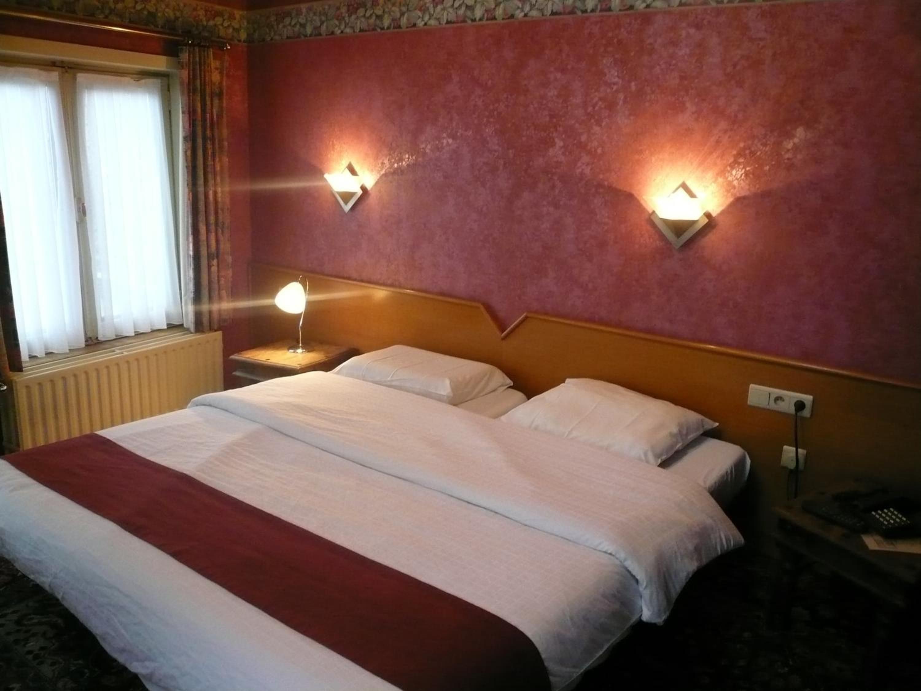 Une chambre d’hôtel avec un grand lit, deux lampes de chevet, une fenêtre avec des rideaux et un radiateur.
