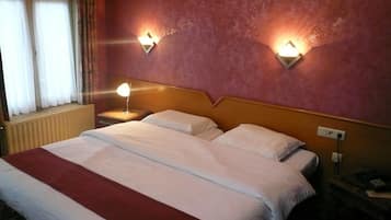 Een hotelkamer met een groot bed, twee bedlampen, een raam met gordijnen en een radiator.