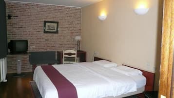 Een hotelkamer met een bakstenen muur, een bed met witte beddengoed en een rode accentkleur, een televisie op een standaard en twee wandlampen.