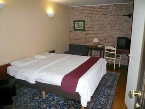 Una habitación de hotel con una cama, un escritorio, un televisor y una pared de ladrillo.
