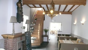 Un restaurante con escaleras, vigas de madera y una araña. Las mesas están dispuestas con copas de vino y cubiertos.