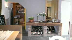 Zona de bar con mostrador de madera, plantas en macetas y estantería para vinos.