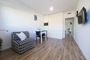 A living room with a patterned sofa, a dining area with a table and chairs, a TV mounted on the wall, and a hallway leading to another room. - Aspio Residence (Camerano)
