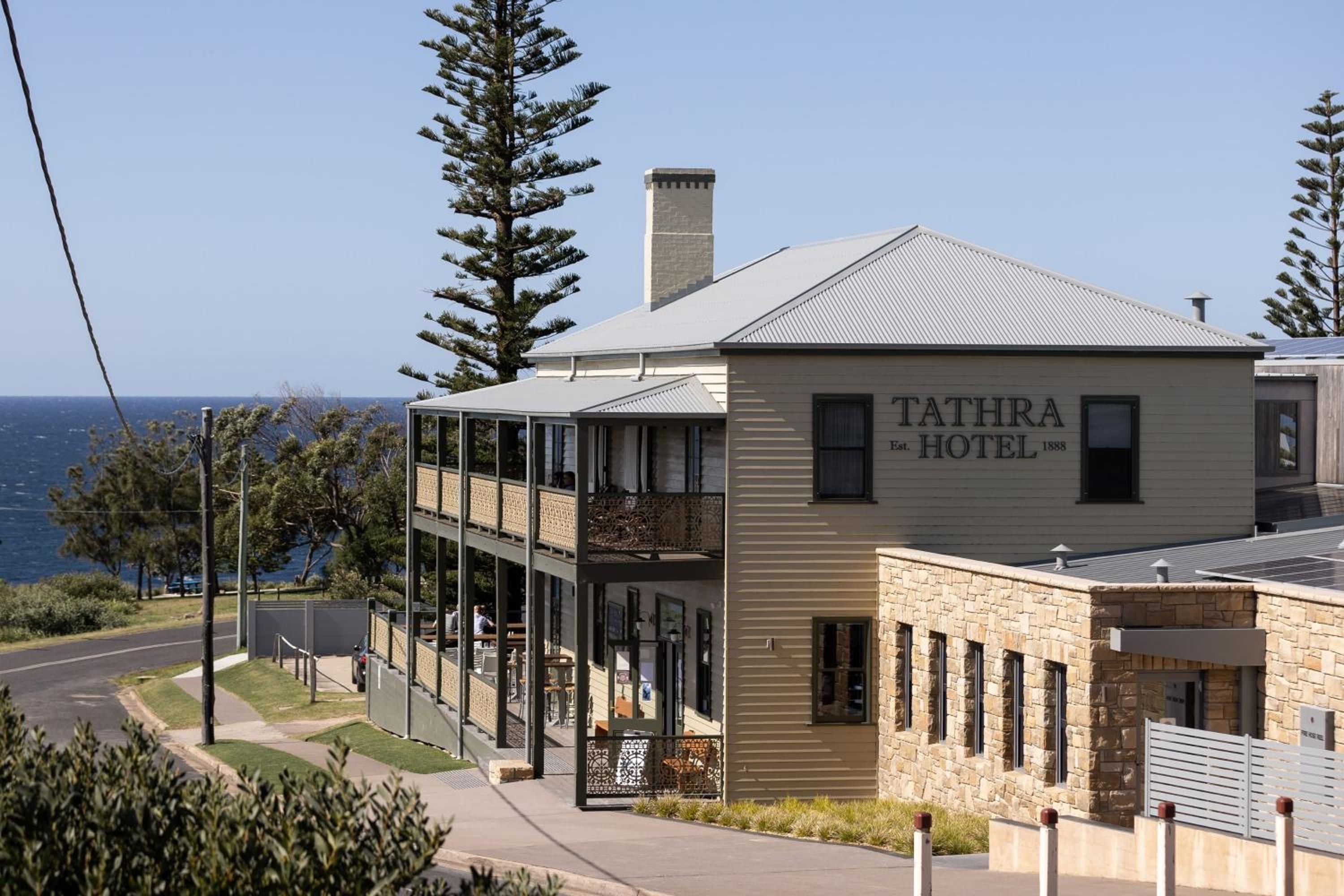A two-story building with a sign reading 'TATHRA HOTEL' and a view of the ocean in the background.