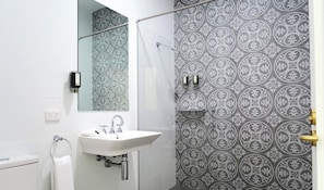 Un baño con lavamanos blanco, espejo y ducha con azulejos estampados.