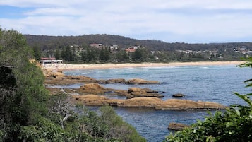 A coastal landscape with rocky shores, a sandy beach, and a forested hill in the background.