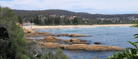 A coastal landscape with rocky shores, a sandy beach, and a forested hill in the background.