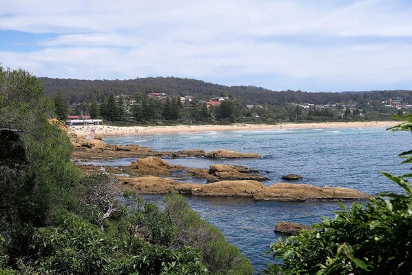 Un paisaje costero con costas rocosas, una playa arenosa y una colina boscosa al fondo.