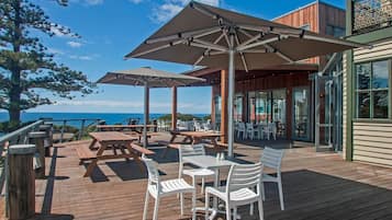 A wooden deck with picnic tables and chairs, outdoor umbrellas, and a view of the ocean.