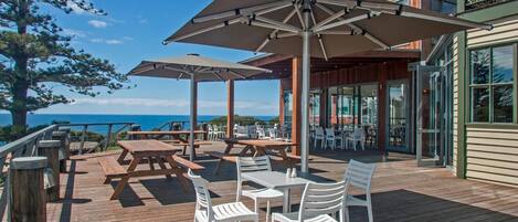 Una terraza de madera con mesas y sillas de picnic, sombrillas y vista al océano.