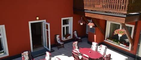 A red building with a balcony, outdoor seating, and hanging flower baskets.