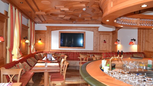 Un interior acogedor con una zona de bar de madera, diferentes disposiciones de asientos y un televisor montado en la pared.
