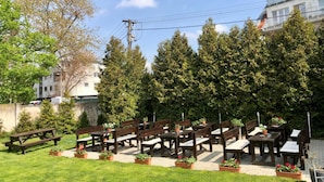 Un espacio al aire libre con mesas y bancos de madera, rodeado de plantas en macetas y árboles.