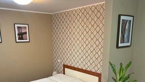 Una cama individual con estructura de madera, una planta en maceta y papel tapiz estampado.