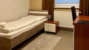 Un dormitorio con una cama individual, una mesita de noche, un escritorio con silla, un radiador y una ventana con cortinas.