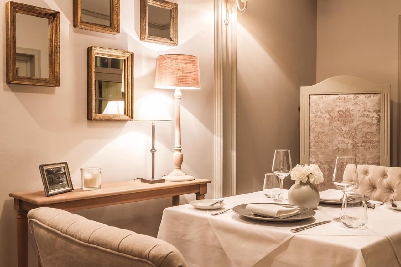 A dining area with a table set for two, a lamp, a mirror, and a framed picture on a wooden side table.