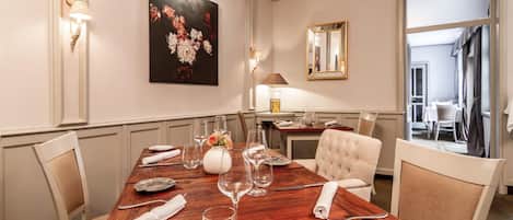 A dining room with a wooden table set for six, surrounded by chairs, a vase with flowers, and a painting on the wall.