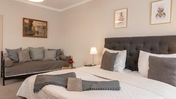 A hotel room with a bed, a sofa, a nightstand, a lamp, and two framed pictures on the wall.