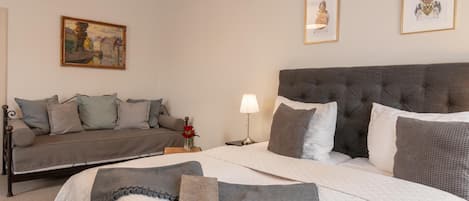 Una habitación de hotel con una cama, un sofá, una mesita de noche, una lámpara y dos cuadros en la pared.