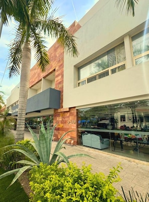 Un edificio moderno con fachada de vidrio, una palmera y un jardín bien cuidado.