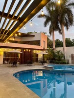 A pool area with a modern building, outdoor seating, and palm trees.