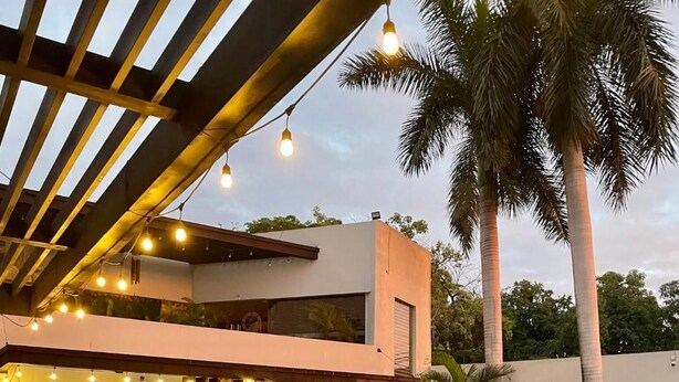 A pool area with a modern building, outdoor seating, and palm trees. - Grann Hotel (Ciudad Valles)
