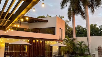 Zona de piscina con un edificio moderno, mobiliario exterior y palmeras.
