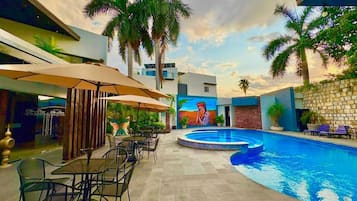 Un área de piscina al aire libre con sillones de descanso, sombrillas y un mural en la pared.